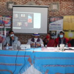 Six representatives of Indigenous communities sitting at a table in front of a projector for Cultural Survival press conference