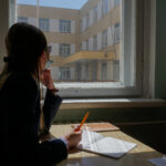 Image of a female high school student from Mongolia looking out a window with a notebook and pen