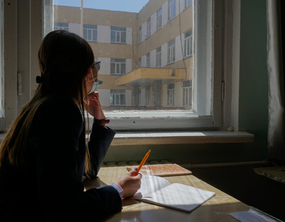 Image of a female high school student from Mongolia looking out a window with a notebook and pen