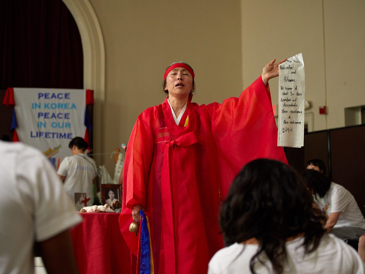 women in red Hanbok (traditional Korean clothing) holding long white paper with black writing