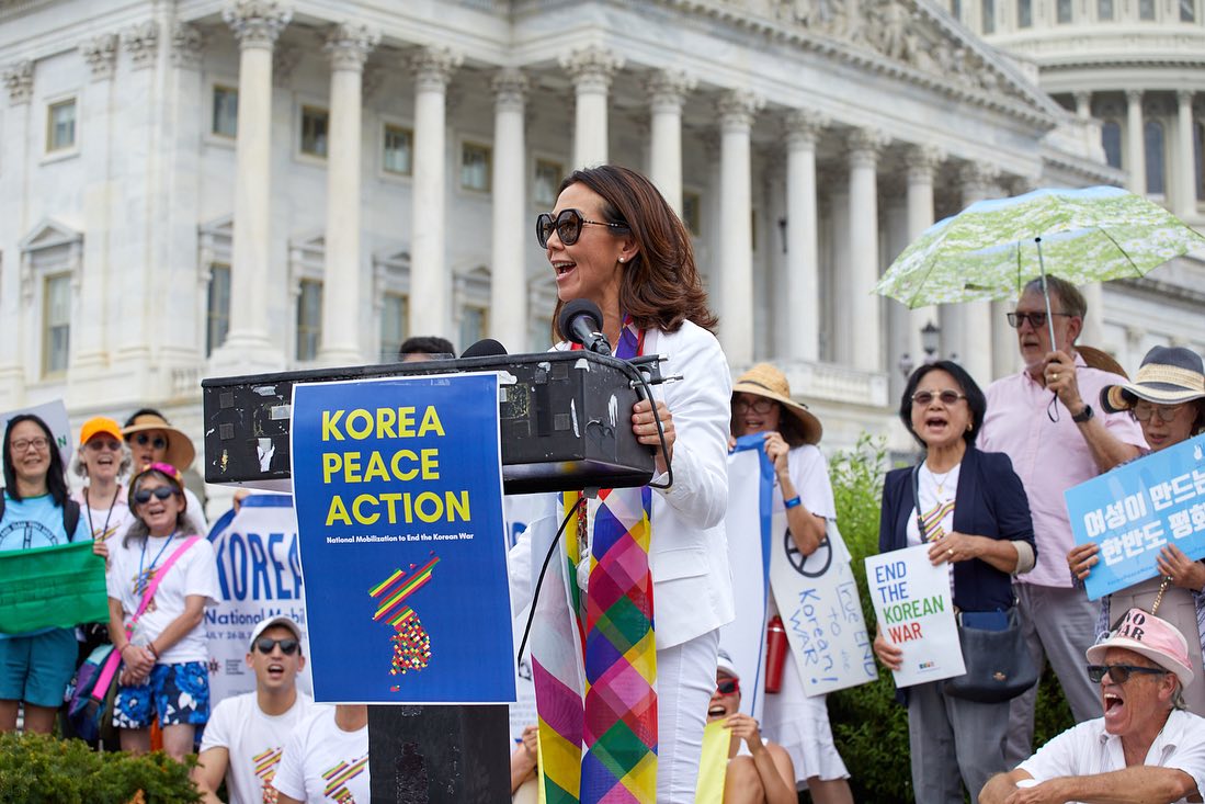 Christine Ahn speaking at podium with poster that states "Korea Peace Action"