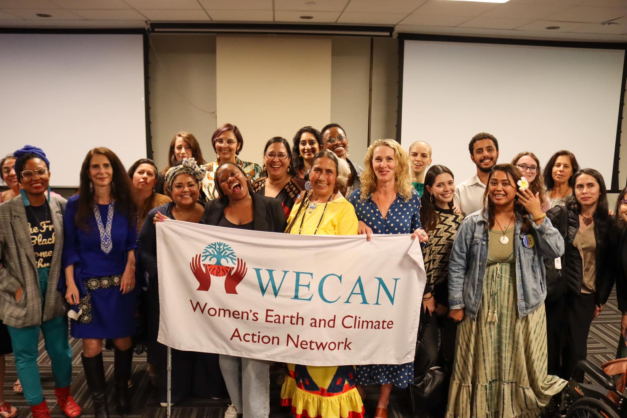 group of people posing for photo with a banner that states "WECAN Women's Earth and Climate Action Network"