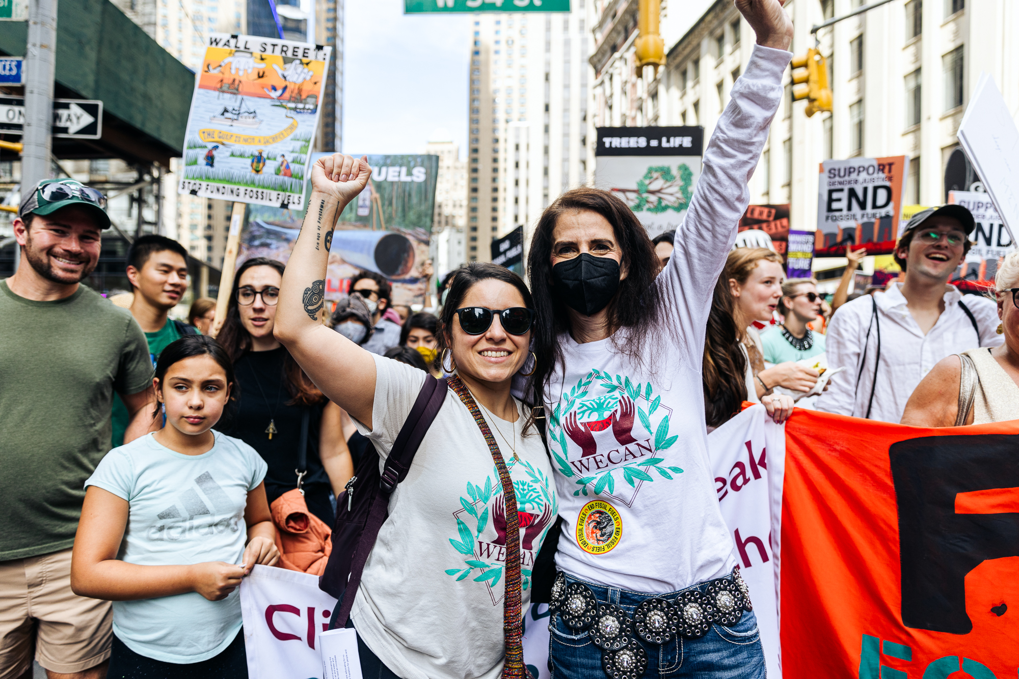 two women with hands above their heads among a crowd of people at a protest